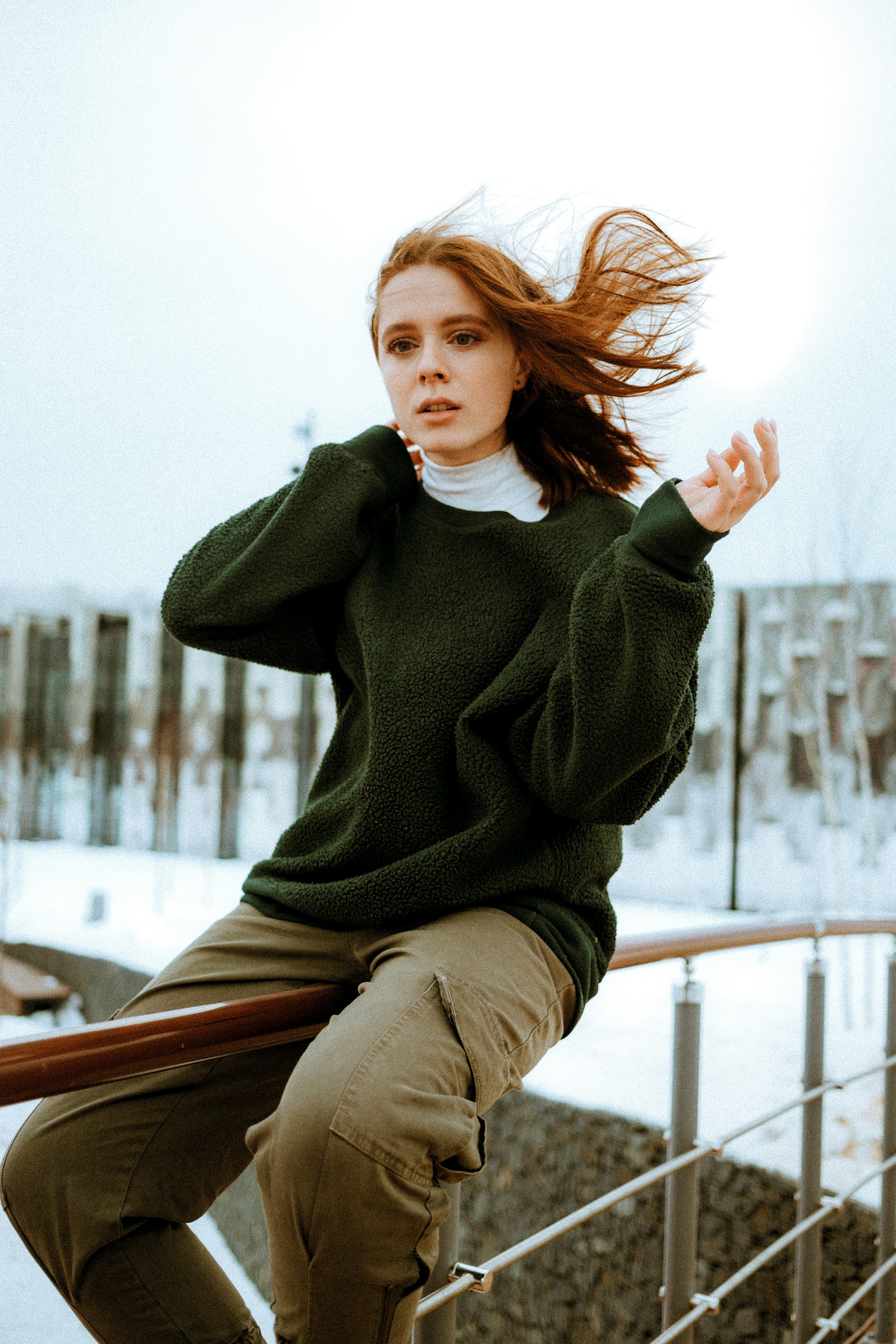woman in green sweater sitting on brown wooden bench during daytime